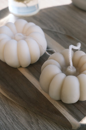 White pumpkin-shaped candles on a wooden surface