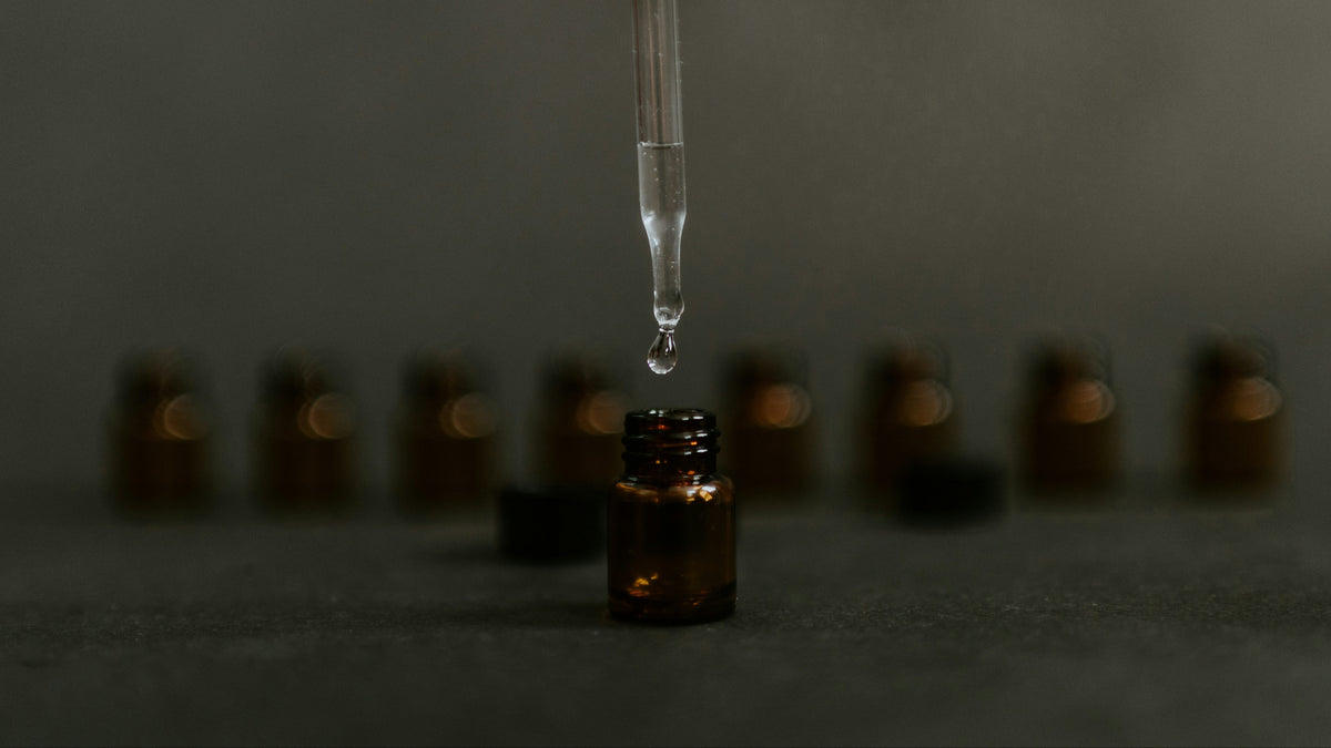 Dropper with a drop over a small brown bottle

